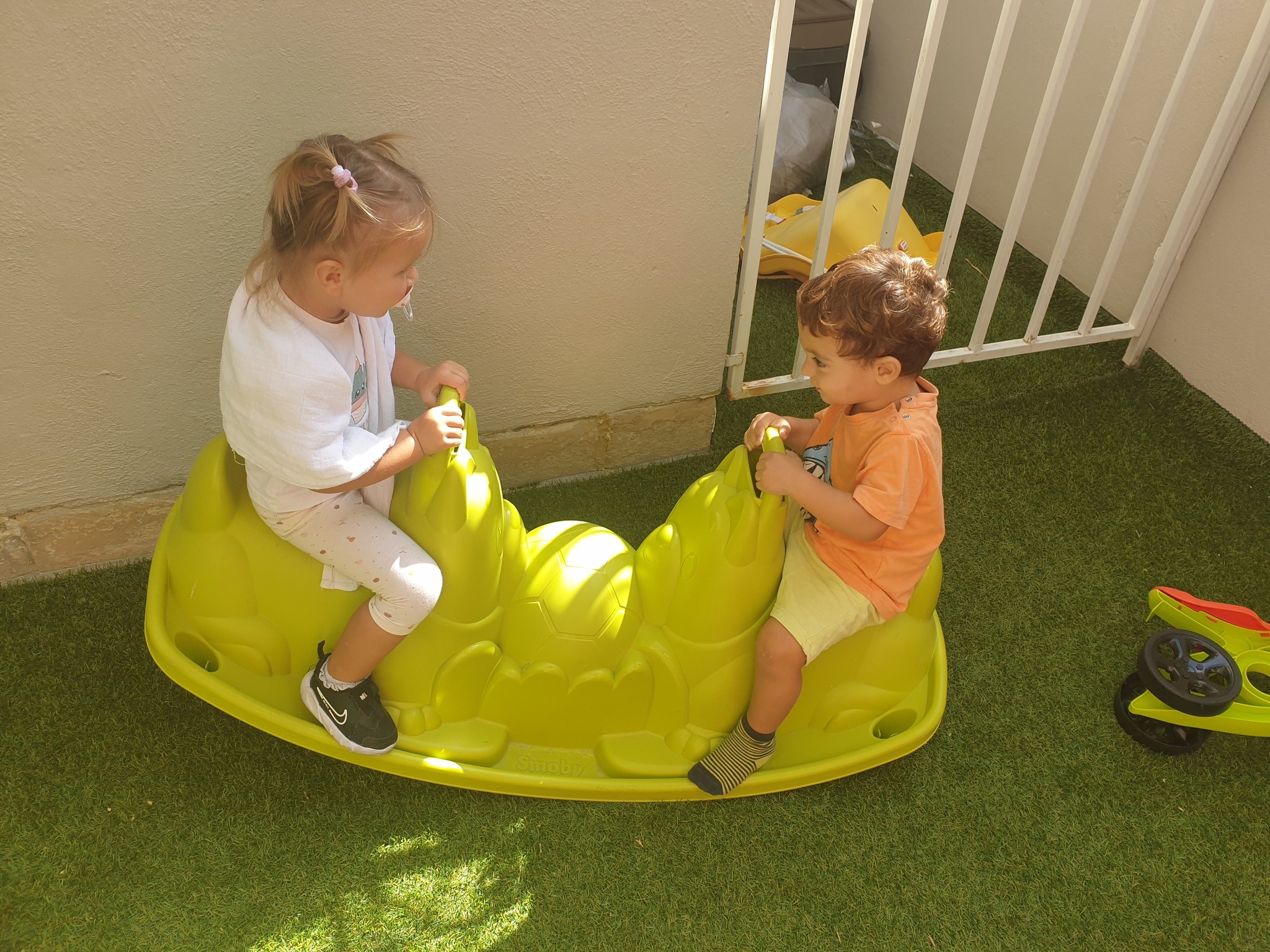 Two children enjoying a shared ride on a green rocker