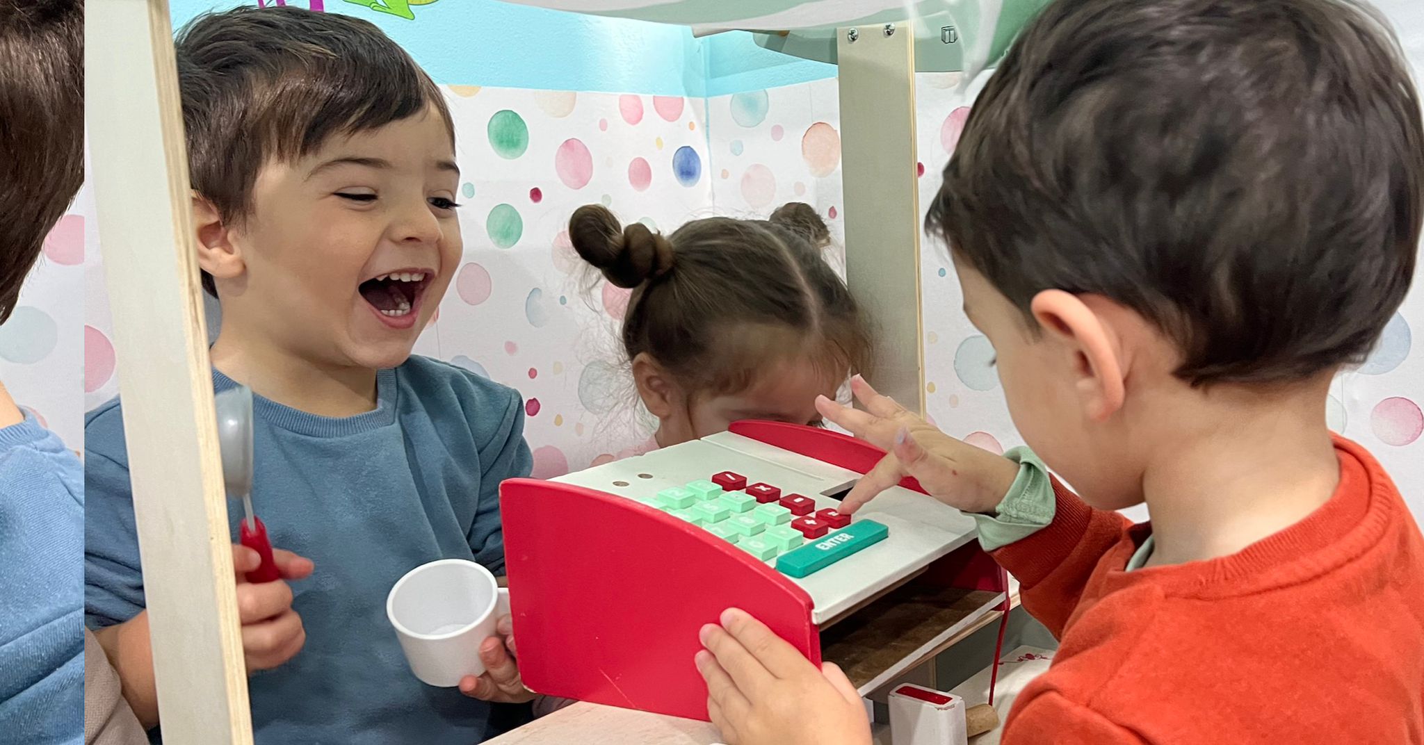 Children engaging in imaginative play at a pretend market, scooping pretend treats and exploring role-play activities